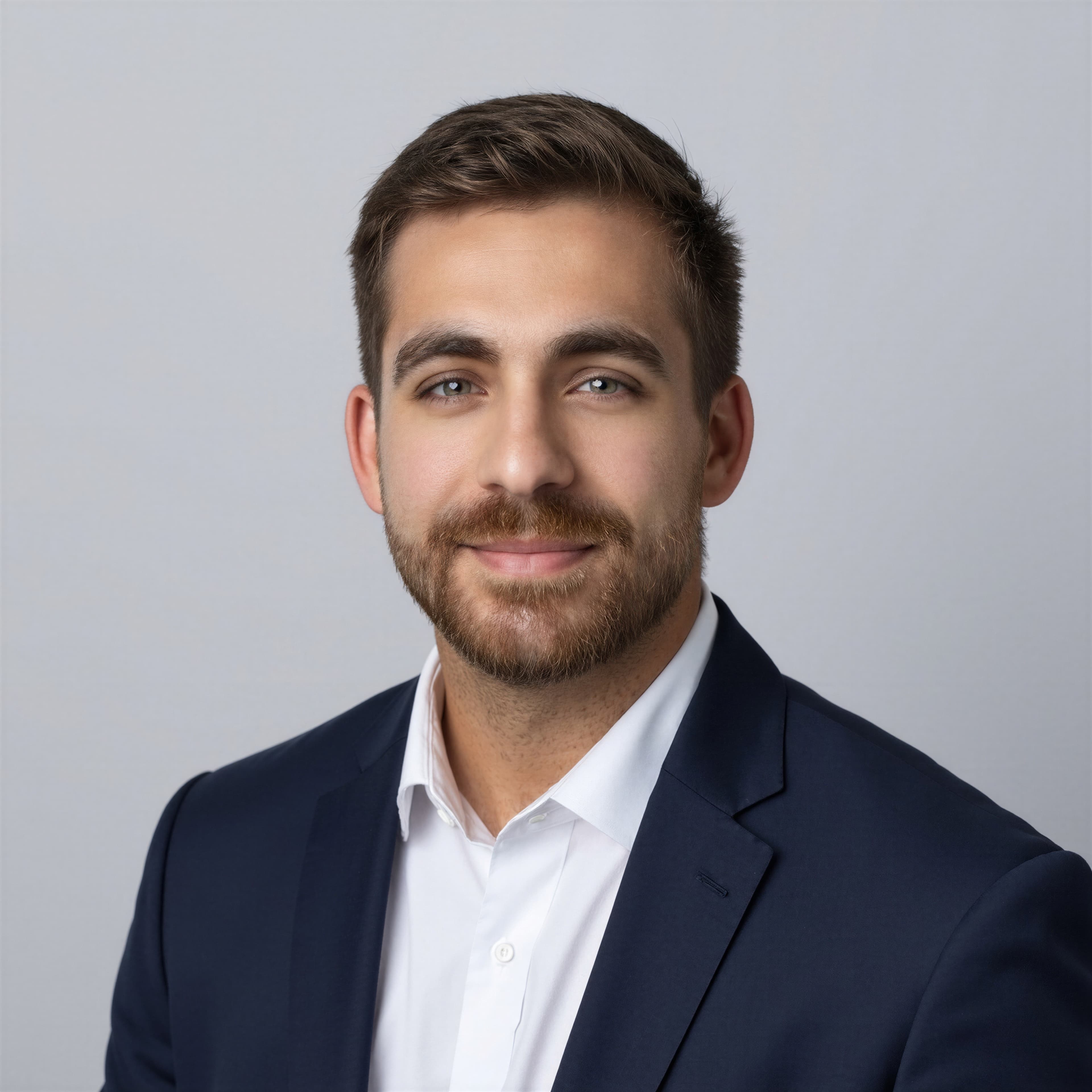 Professional headshot of a bearded man wearing a navy blue suit and white dress shirt.