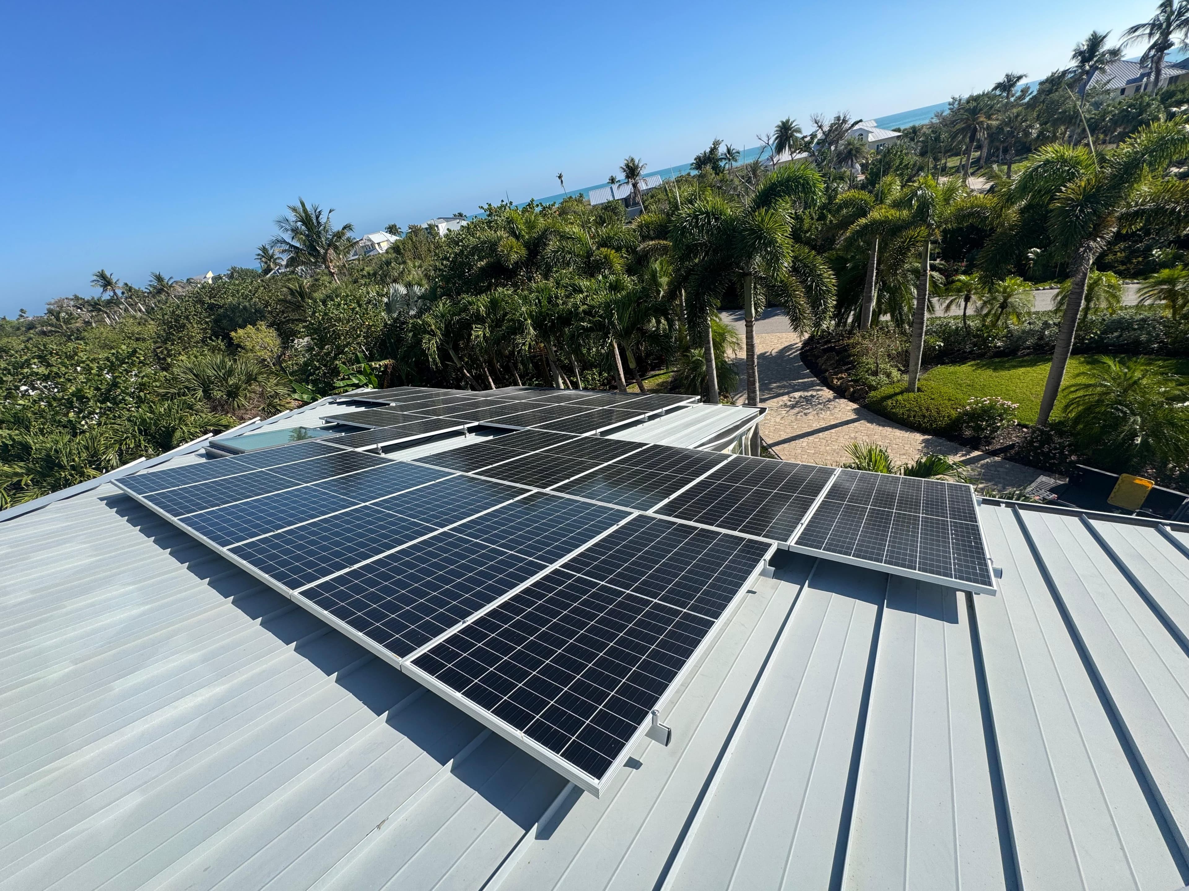 Solar panels on a metal roof overlooking a tropical landscape with palm trees and ocean.